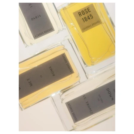 Four rectangular glass perfume bottles with yellow and white labels arranged diagonally against a plain background