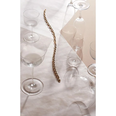 An overhead still life composition featuring a gold chain necklace arranged among several empty glass goblets and champagne flutes.