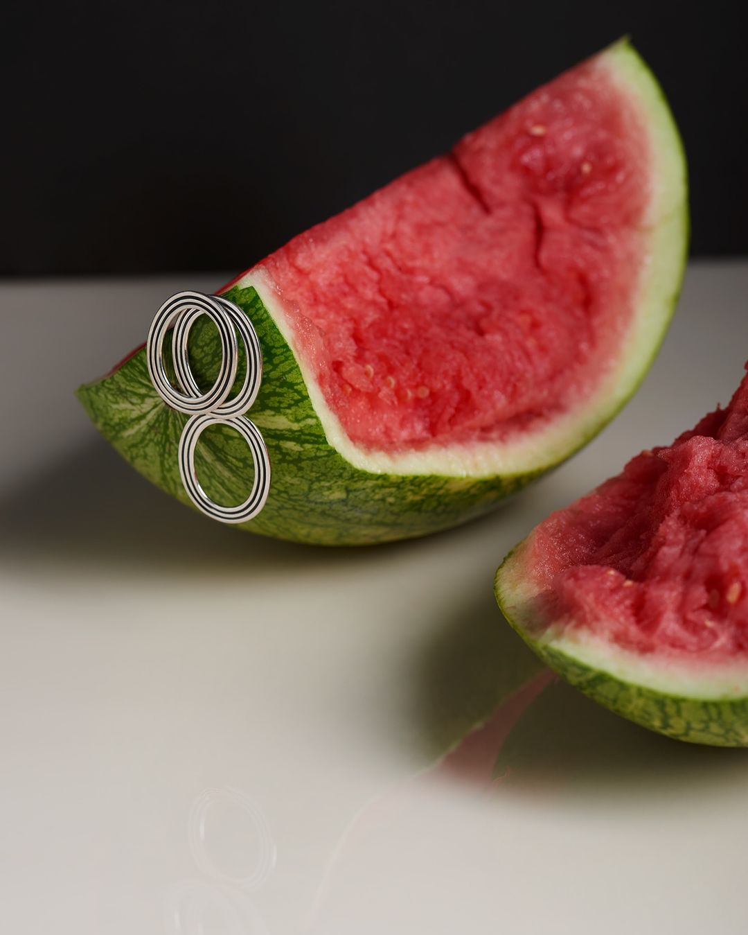 A slice of fresh watermelon is showcased with circular decorations against a contrasting dark background on a reflective surface.