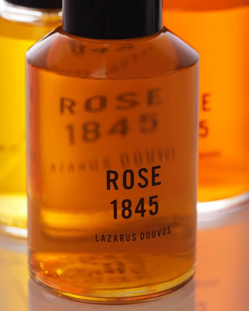 Close-up shot of a Lazarus Douvos Rose 1845 fragrance bottle featuring a gold-colored liquid inside with black text on the bottle.