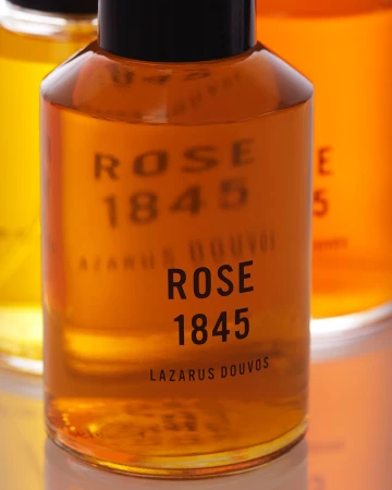 Close-up shot of a Lazarus Douvos Rose 1845 fragrance bottle featuring a gold-colored liquid inside with black text on the bottle.