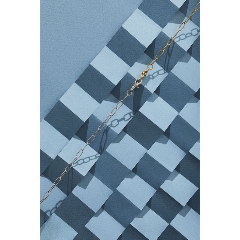 Still life photograph of a gold chain on a geometric surface with blue and gray tones. The chain is displayed diagonally across the frame.