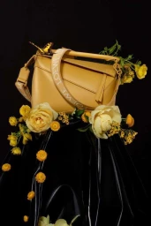 Yellow Loewe Puzzle bag resting on shiny black material adorned with yellow roses and a small metallic butterfly.