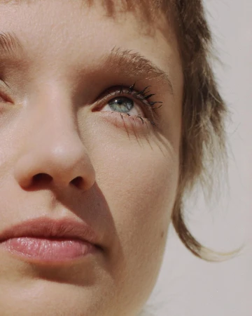 Close-up portrait of a woman with short textured hair and blue eyes looking upwards under natural light by Gaia Bonanomi.