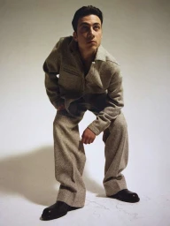 Man wearing a textured grey jacket and matching trousers posing against a light background by photographer Gaia Bonanomi