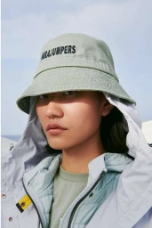 Close-up portrait of an East Asian woman wearing a light green bucket hat with black text and a white hooded jacket