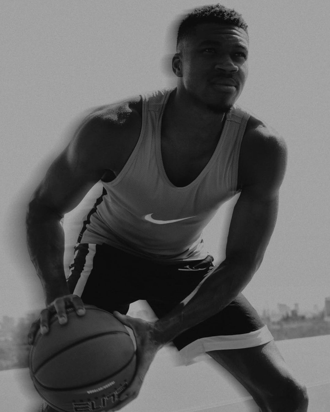 Monochrome portrait of an adult male athlete dribbling a basketball outdoors, wearing a tank top and shorts, athletic pose, with soft focus.