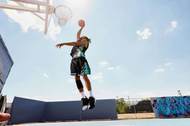 Basketball player mid-air dunking a basketball on an outdoor court under a bright clear sky, photographed by Garrett Byrum.