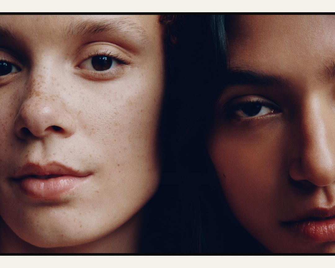 Close-up portrait featuring two women with contrasting skin tones, showcasing detail on their facial features, and a minimalistic aesthetic.