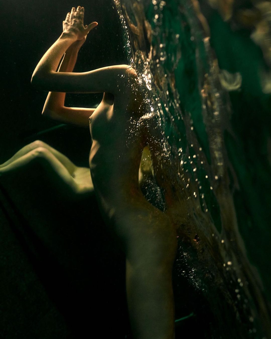 Artistic portrait of an adult female in shallow water with arms raised overhead. The portrait exhibits visual effects and green dominant hues.