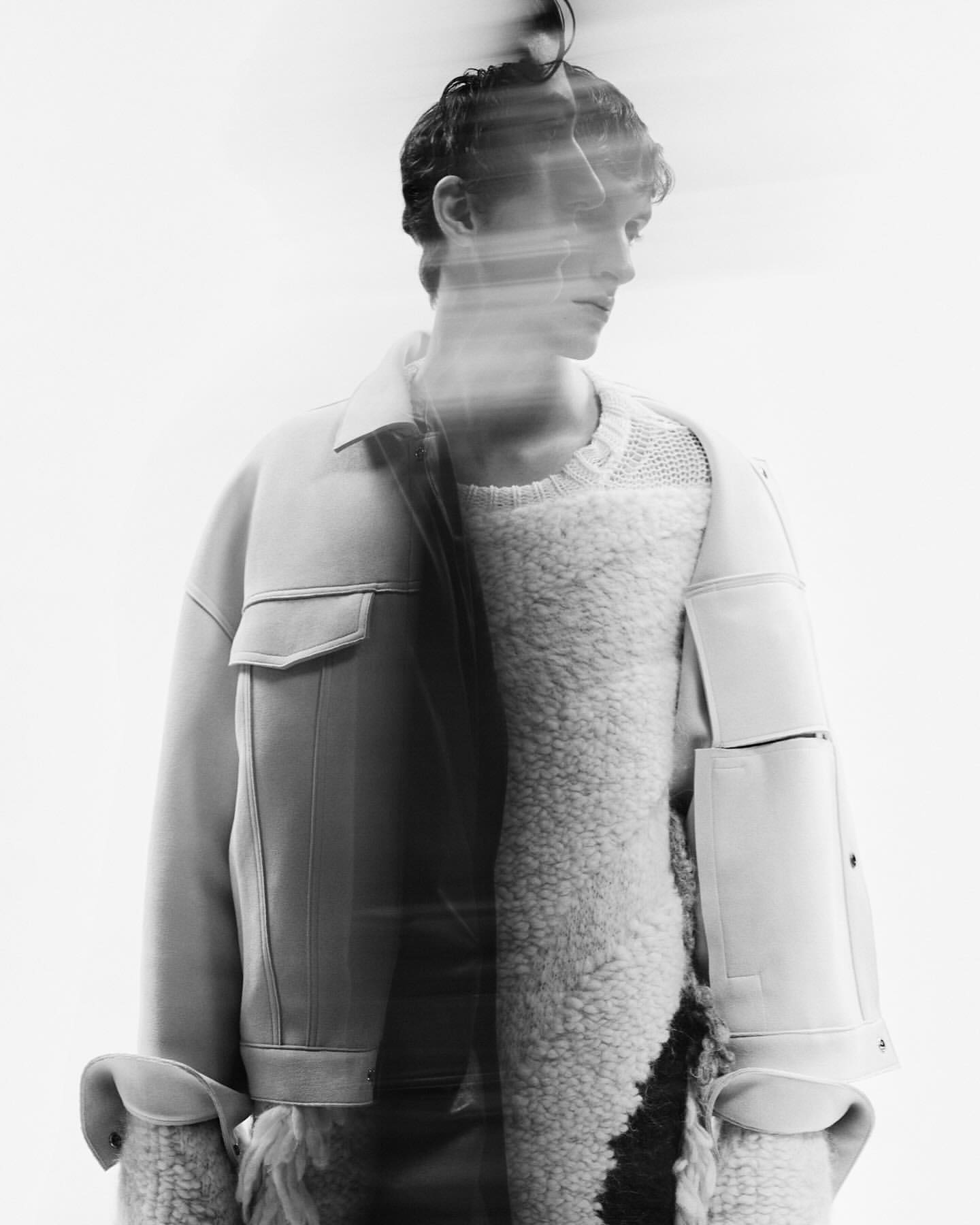 Black and white studio shot of a man in a light jacket over a fuzzy sweater, artistic motion blur effect and soft, diffused lighting.