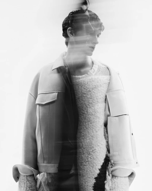 Black and white studio shot of a man in a light jacket over a fuzzy sweater, artistic motion blur effect and soft, diffused lighting.