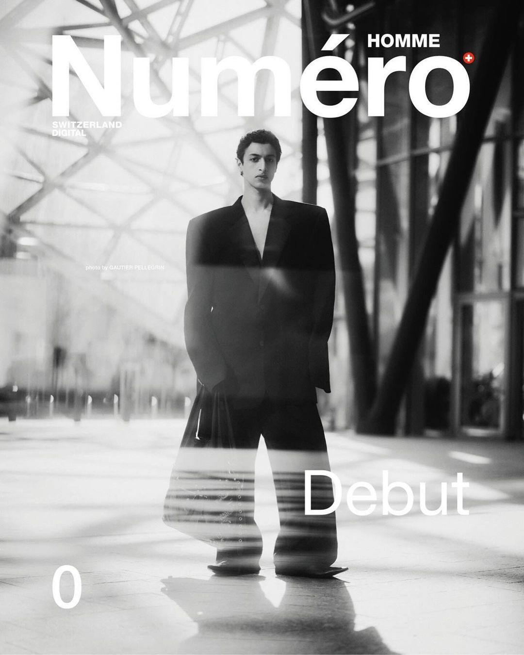 Black and white fashion magazine cover featuring a male model in a suit, set against a blurred architectural background with prominent magazine text.