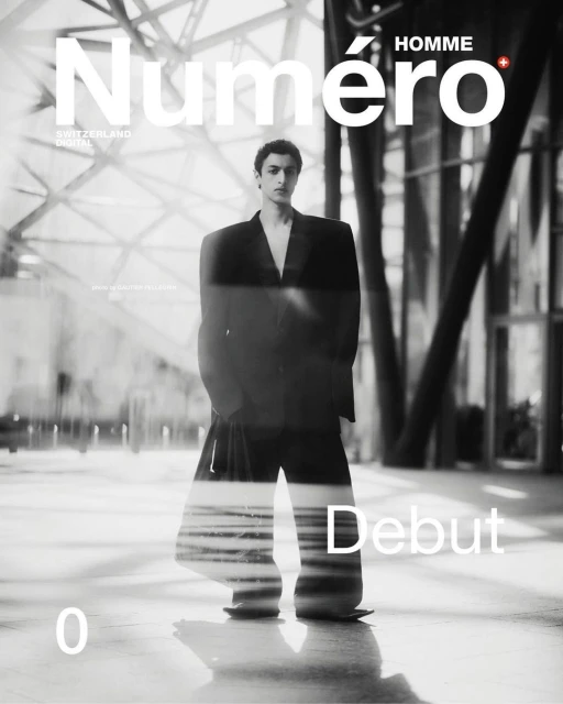 Black and white fashion magazine cover featuring a male model in a suit, set against a blurred architectural background with prominent magazine text.
