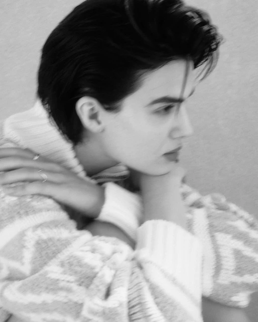 Black and white portrait of a young woman with dark hair, wearing a patterned sweater, resting her chin on her folded hands.