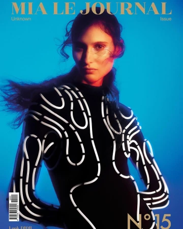Model in a black long-sleeve top with white abstract piping against a vibrant blue background with warm red rim lighting.