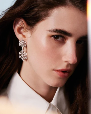 Close-up portrait of a woman wearing ornate floral diamond drop earrings and a white buttoned shirt shot by Gautier Pellegrin.