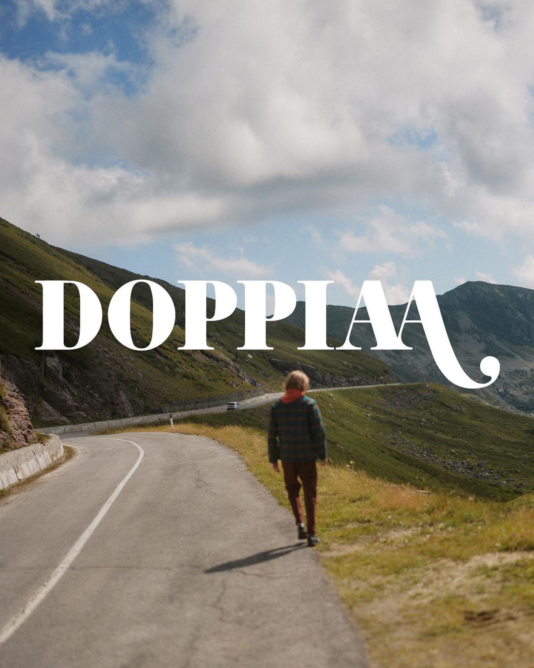 Person walking on a winding road through green hills under a cloudy sky; landscape with mountains in the distance and large text overlay.