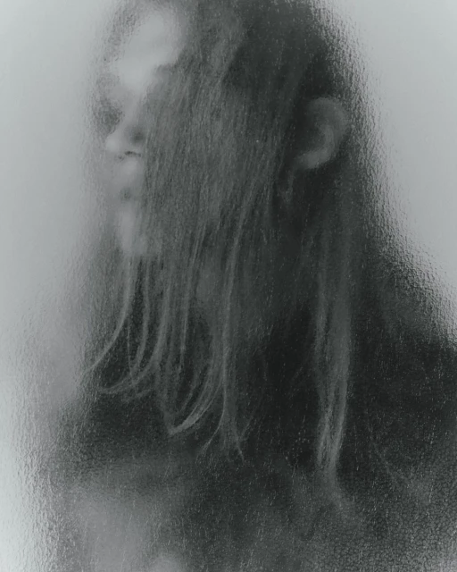 Monochromatic portrait of an individual with long hair, partially obscured by a textured glass or vapor effect, creating an ethereal mood.