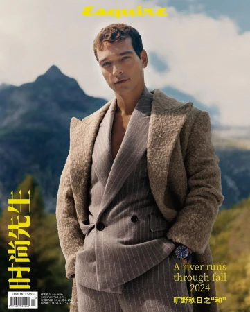 Man wearing a textured wool coat and pinstriped suit standing outdoors against a mountain background.