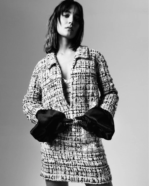 A fashionable woman posing indoors wearing a patterned tweed jacket and matching mini dress with black satin gloves in a studio setting.