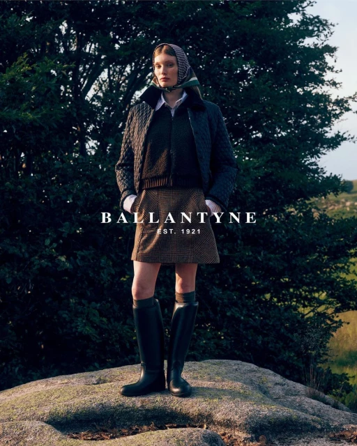 Woman poses outdoors wearing a quilted jacket, plaid skirt, knee-high boots, and a scarf. The brand name BALLANTYNE is in the foreground.