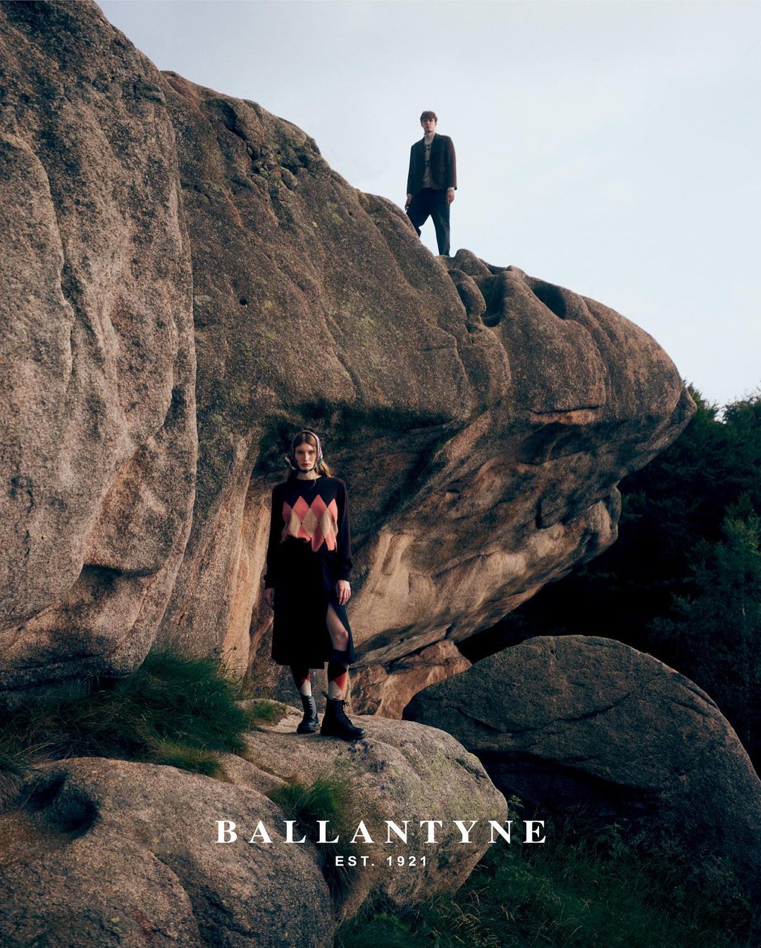 Two models standing on rugged rocky formations outdoors under an open sky, captured by Gautier Pellegrin in Milan.