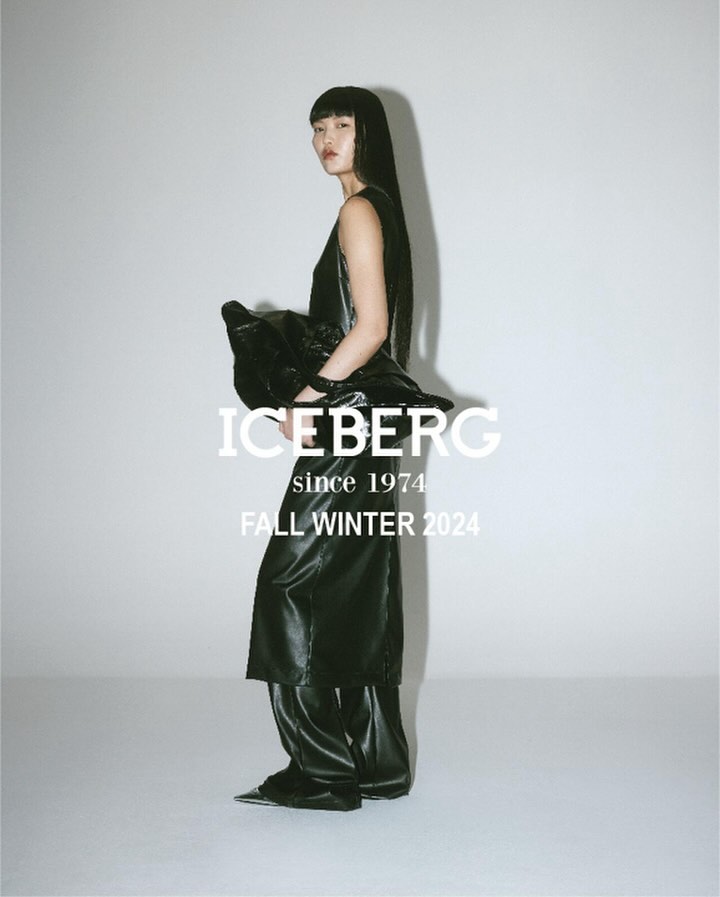 A woman poses in black Iceberg Fall/Winter 2024 fashion in a studio with a white backdrop. She wears a dark top, long skirt and pants.