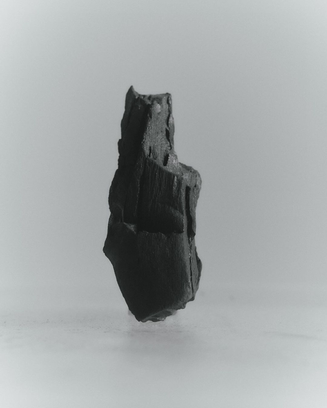 Monochromatic shot of a textured, irregularly-shaped charcoal piece against a gradient gray backdrop, highlighting its unique form.
