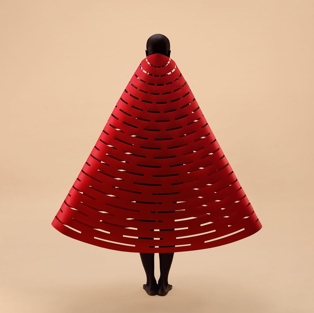 Person in a striking red, cone-shaped dress with horizontal slits, viewed from the back against a light beige background in a studio setting.