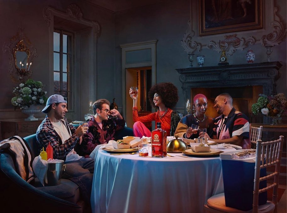 Five diverse adults at a round table in an ornate dining room with a bottle of Jagermeister, drinks, food, and a festive, celebratory mood.