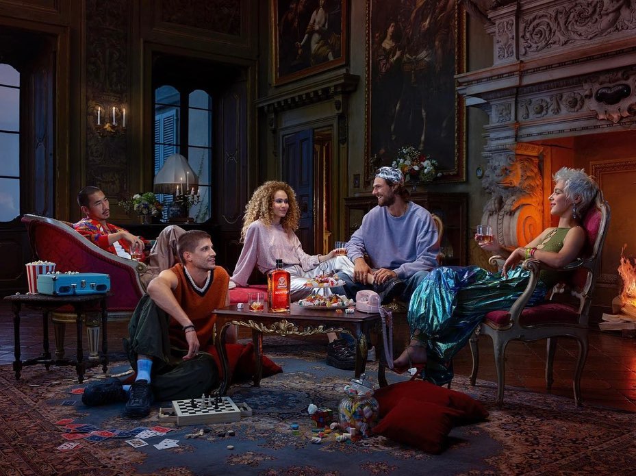 A diverse group of friends relaxing in a vintage interior with ornate décor, gathered around a low table filled with snacks and drinks.