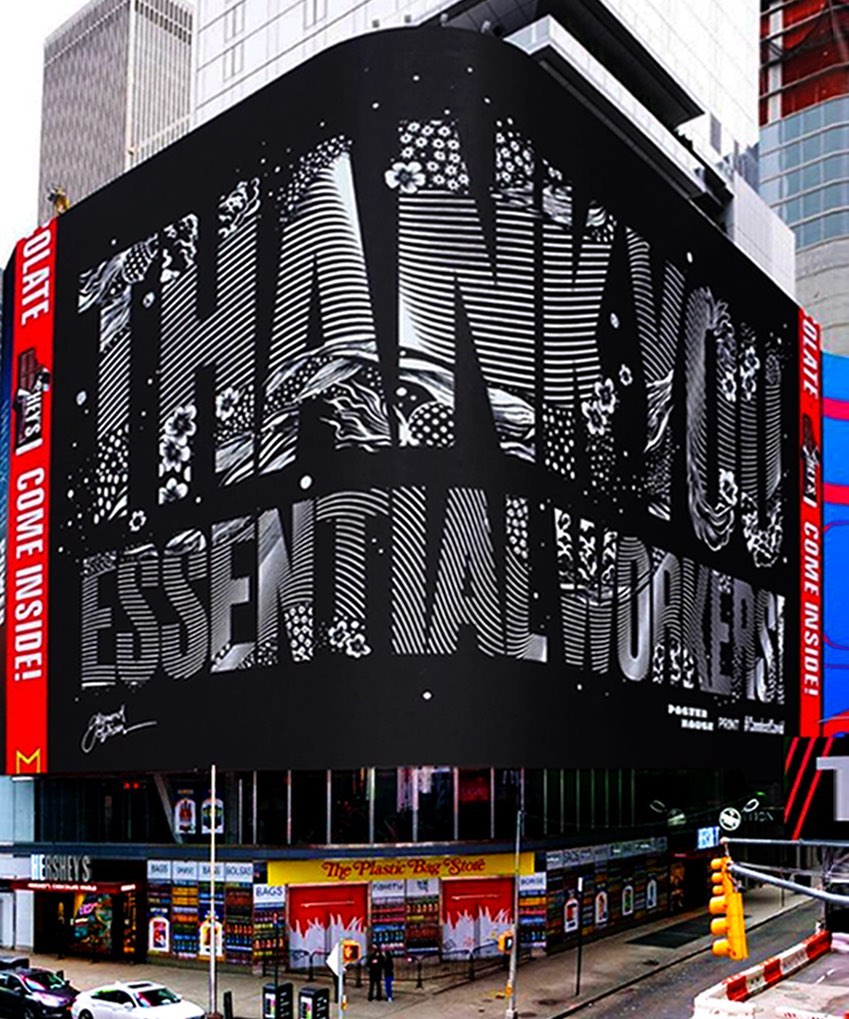 Outdoor view of a large-scale black and white mural in Times Square that thanks essential workers above the storefronts on a city street.