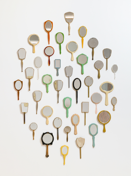 Overhead shot of many colorful vintage handheld mirrors arranged in a circle against a clean white background in a studio setting.