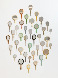 A collection of vintage hand mirrors with varied pastel and metallic frames arranged in a diamond pattern on a white wall.