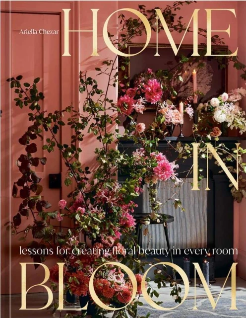 Floral-themed book cover featuring blooms, vines, and elegant typography, set against a coral wall with a fireplace and candle decor.