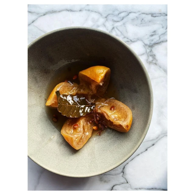 High-angle shot of a bowl of preserved lemons with bay leaf, with a gray bowl against a white marble background, food and beverage.