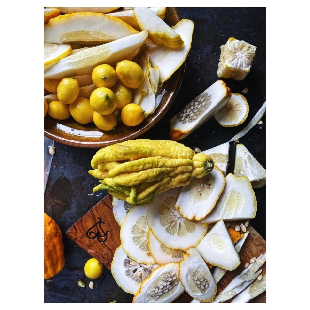 Overhead shot of sliced and whole Buddha's hand fruit and lemons arranged on a dark surface, some on a wooden cutting board.