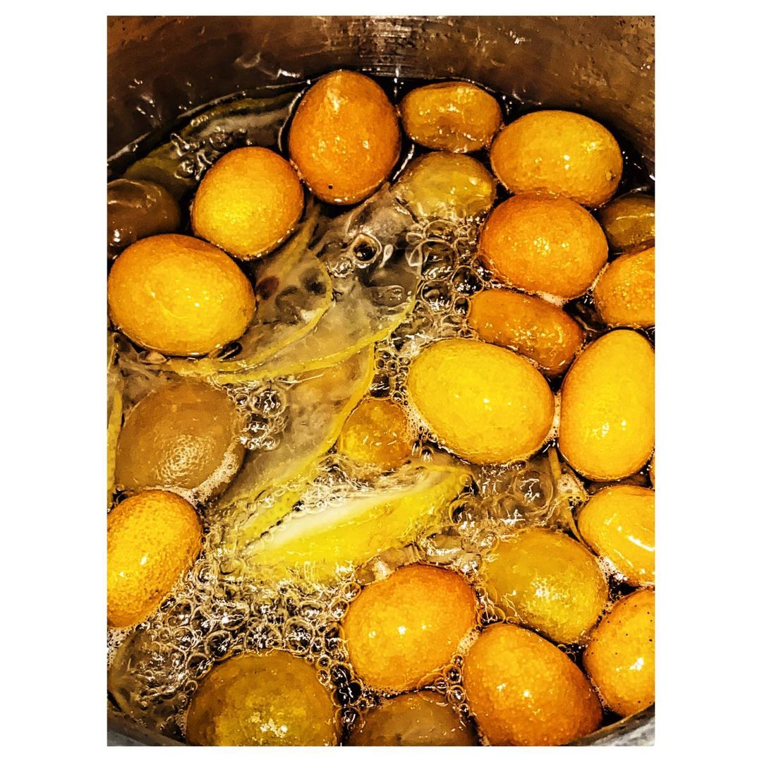 Close-up overhead shot of candied kumquats simmered in a pot, featuring a warm color palette with oranges, yellows, and golden hues.