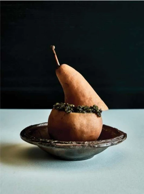 Still life shot of two pears, one partially sliced, sitting on a shallow plate against a dark background in warm, inviting light.