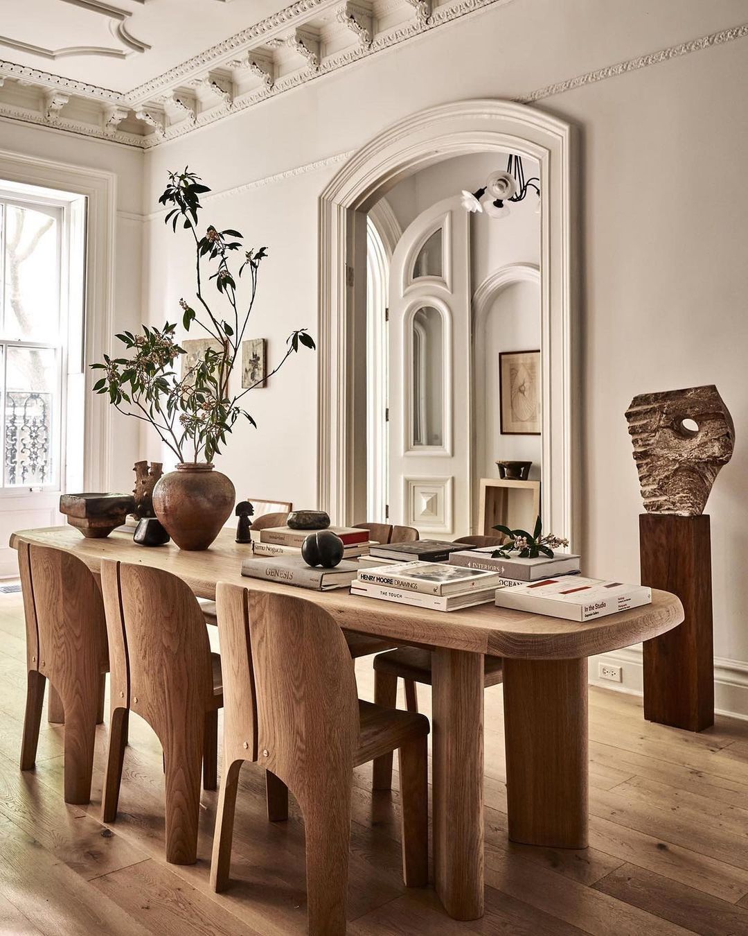 Interior of a dining room featuring a wooden table and chairs, a decorative vase with branches, and neutral wall colors.