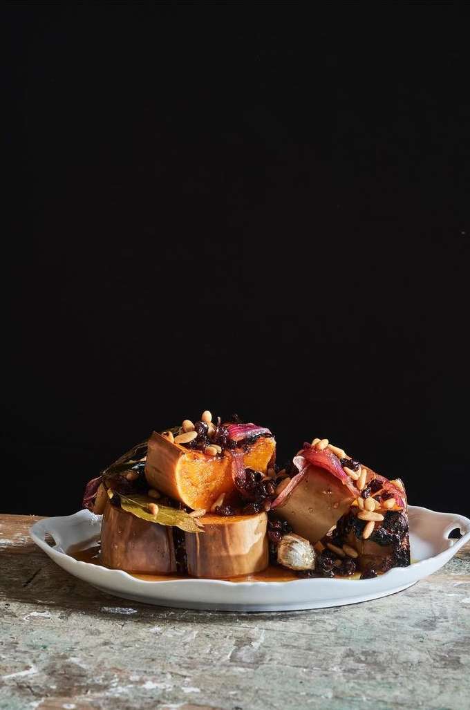Stacked root vegetables on a white plate, arranged against a black background, showcasing culinary presentation and healthy ingredients.