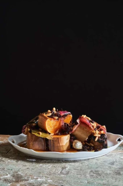 Stacked root vegetables on a white plate, arranged against a black background, showcasing culinary presentation and healthy ingredients.