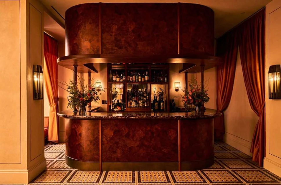 Ornate bar with stocked shelves of liquor, floral arrangements, and low lighting in a classic interior setting.