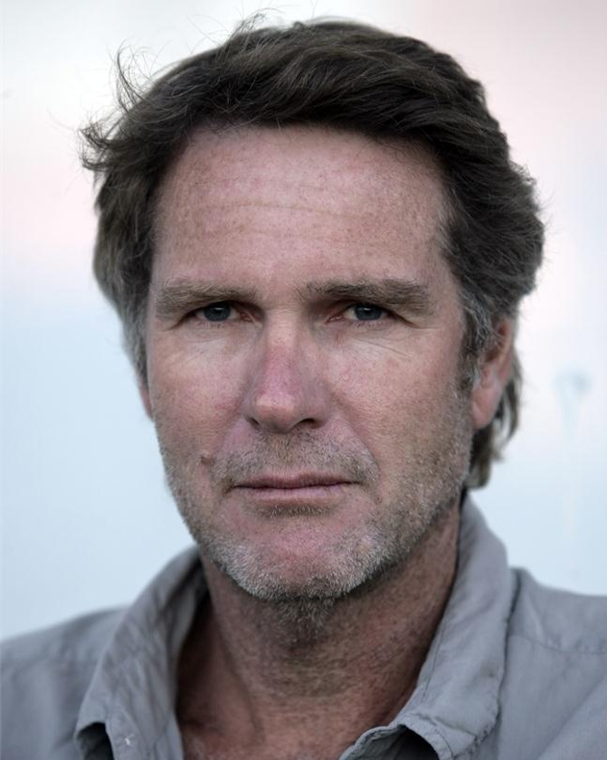 Headshot portrait of an adult male with light brown hair and a neutral facial expression against a soft, light background.
