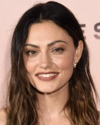 Close-up portrait of actress Phoebe Tonkin smiling with long dark hair and gold earrings against a light pink background