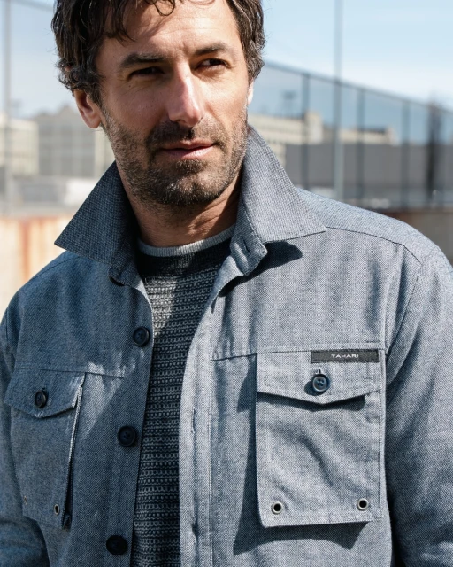 Portrait of a middle-aged man in a blue button-down jacket outdoors, with a modern building in the background and soft natural light.