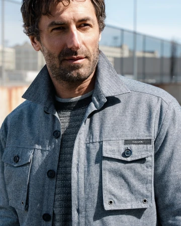 Portrait of a middle-aged man in a blue button-down jacket outdoors, with a modern building in the background and soft natural light.