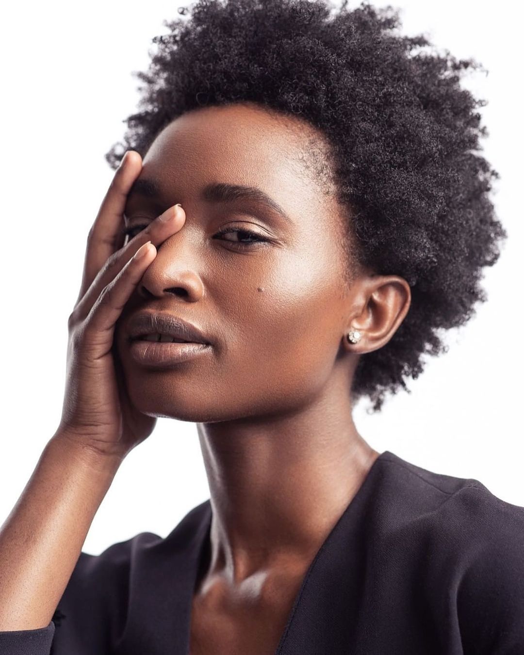 Close-up portrait of a woman with an afro hairstyle, wearing a black top against a bright white background in a studio setting.