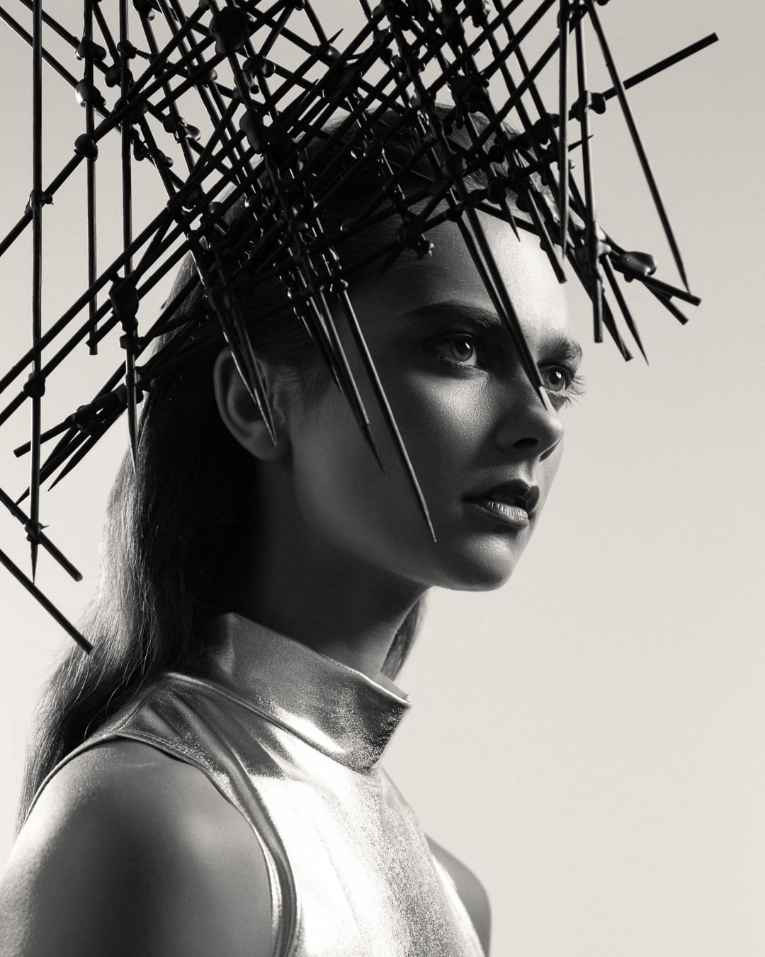 Monochrome portrait of a woman with creative headwear, gazing away from the camera in a studio setting with soft lighting.